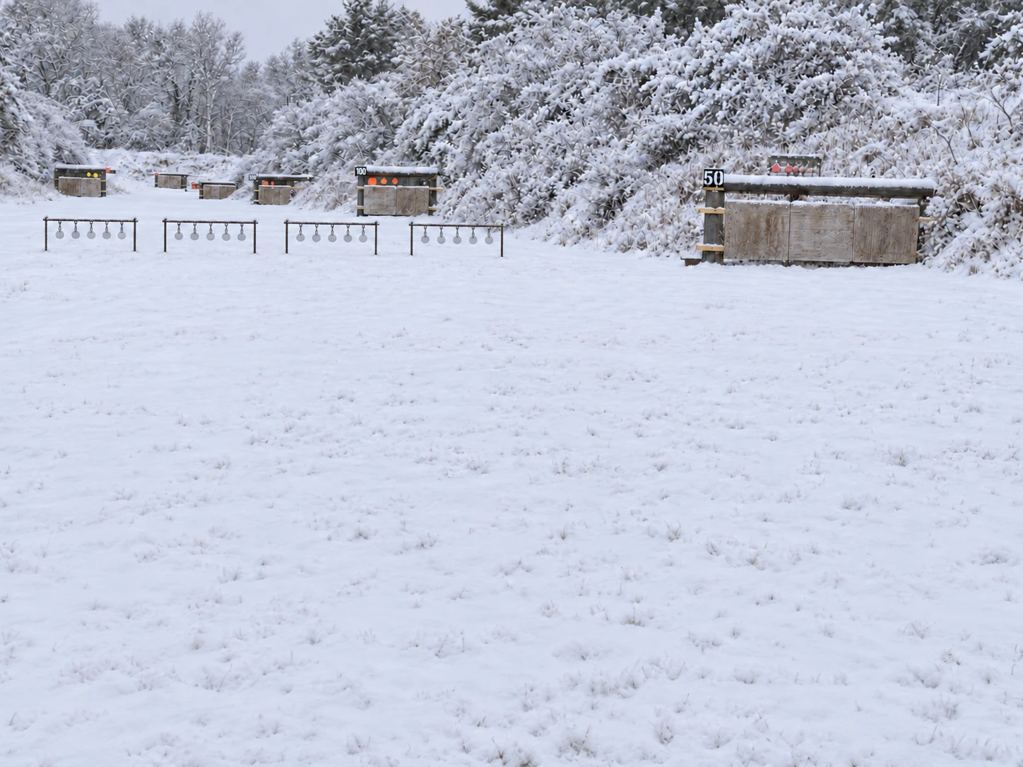 The rifle range under snow: four racks of five 4-inch metal targets set out in front of the berm, with the 50 and 100 yard target banks behind